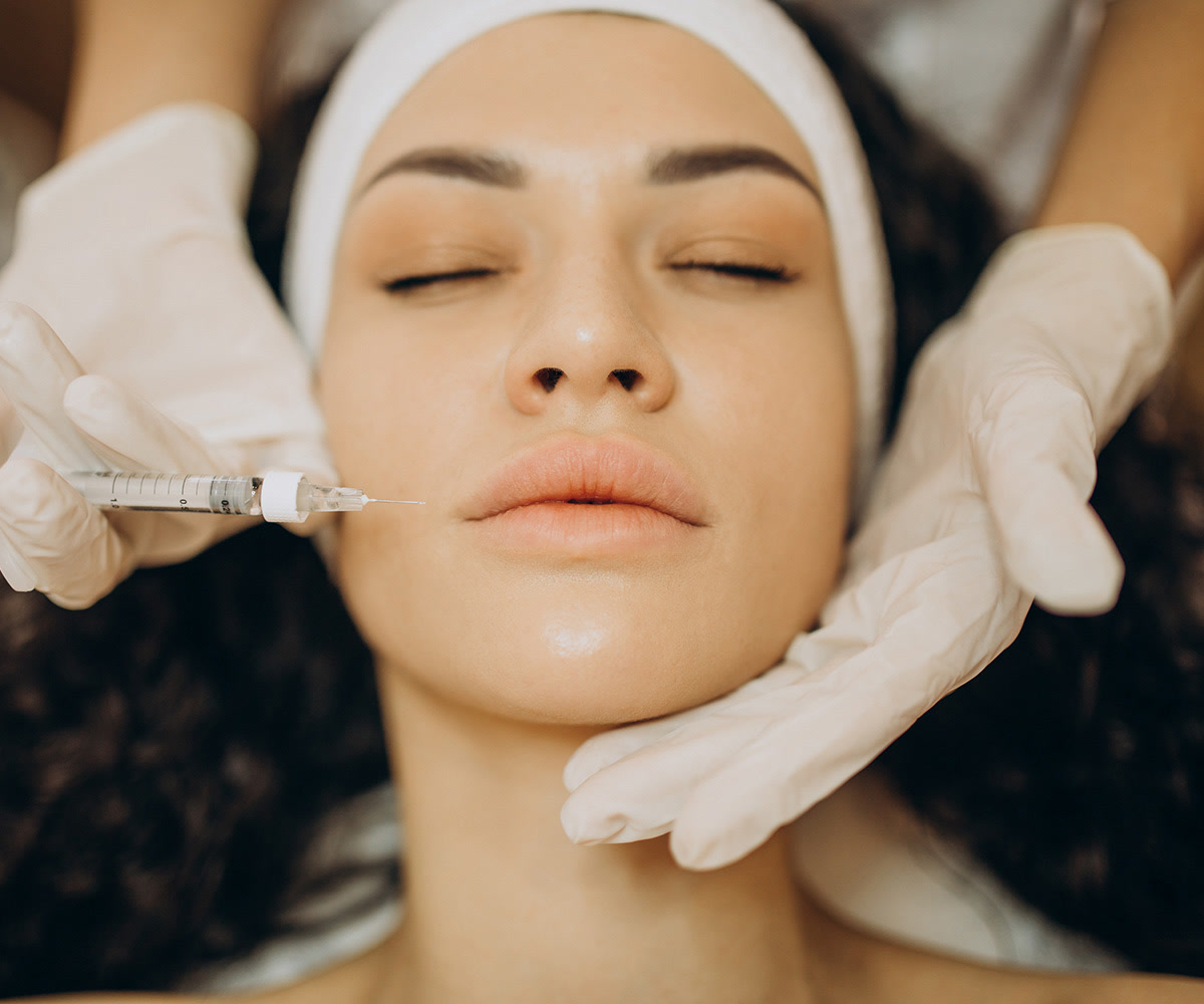 Woman receiving a facial injection near the lip area while lying on a treatment bed