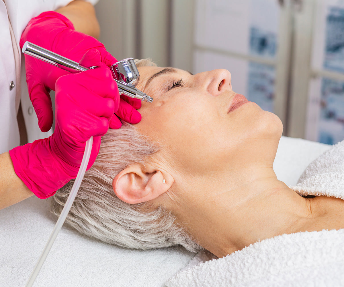 Woman receiving an airbrush facial while reclined on a spa bed